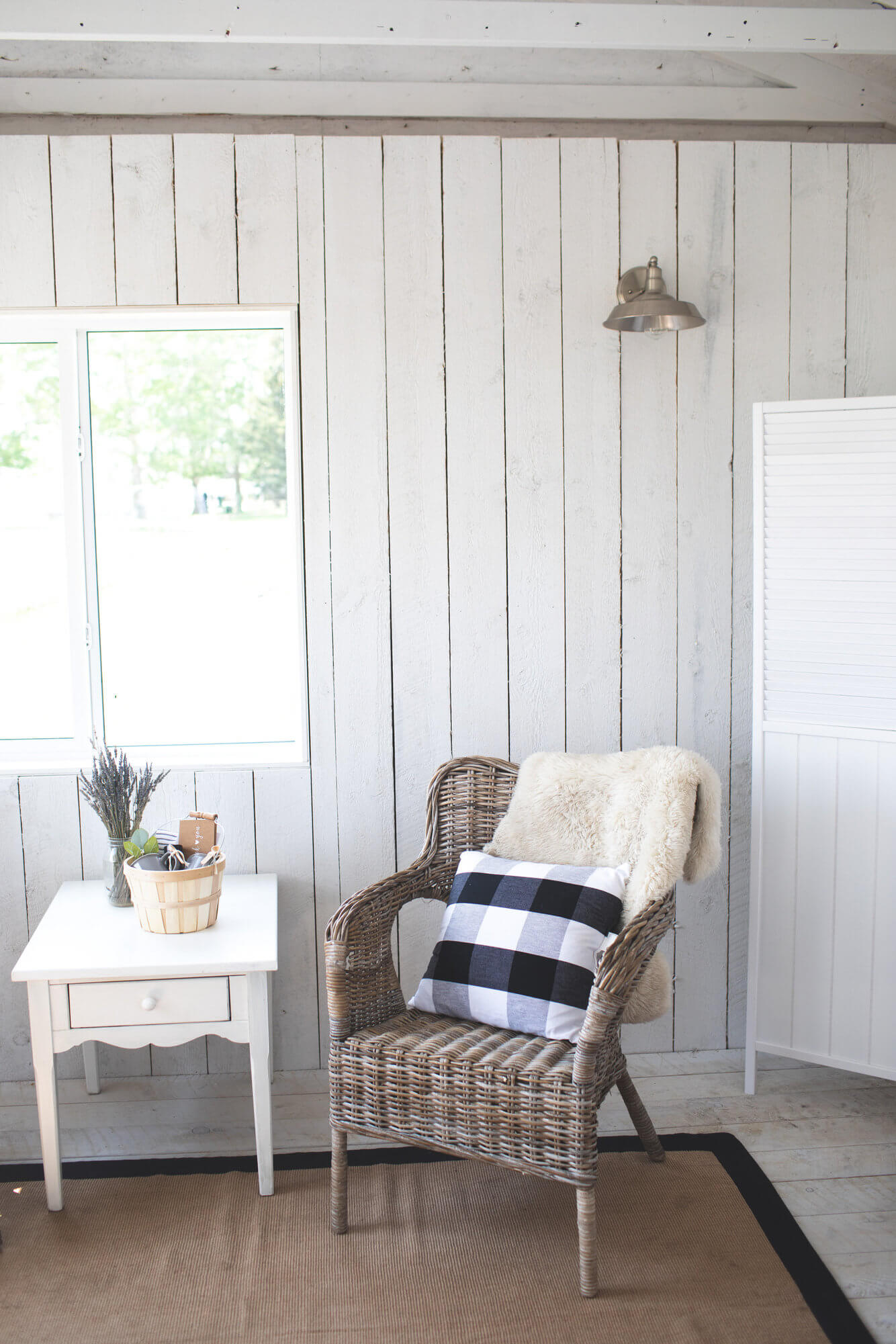 garden cottage cottage white wood walls, a wicker chair with a plaid pillow, a white side table with lavender on it
