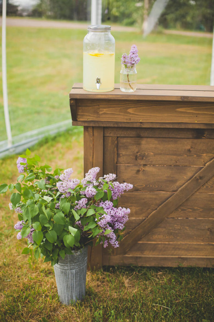 lilacs in a metal bin, juice and flowers sitting on a wood bar