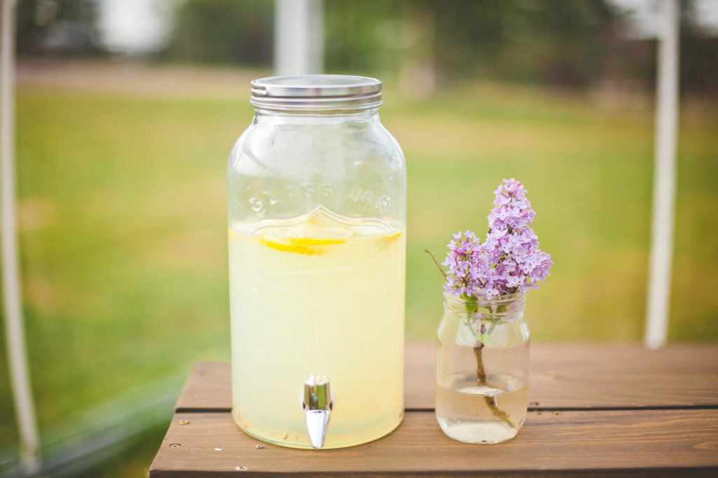 juice dispenser of lemonade with a mason jar of lilacs beside